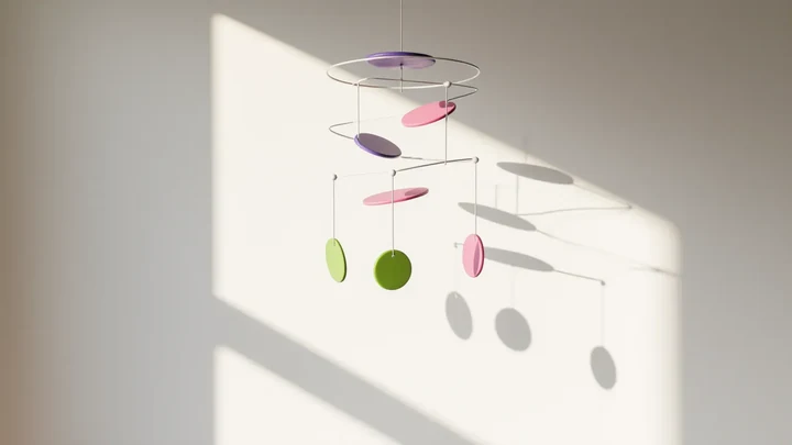 A white mobile of lime, pink and violet discs hanging still in a bright room